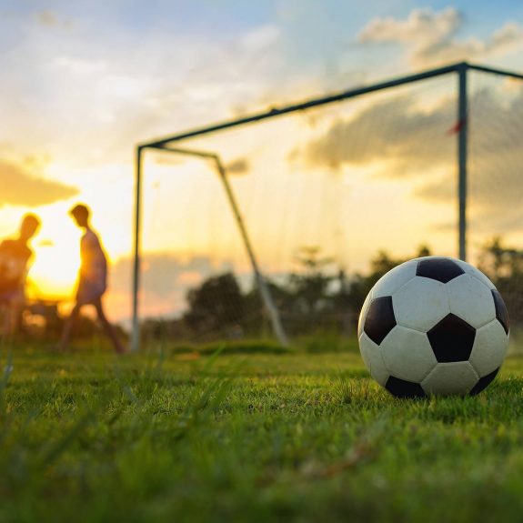 Kids Playing Football In Community At Sunset